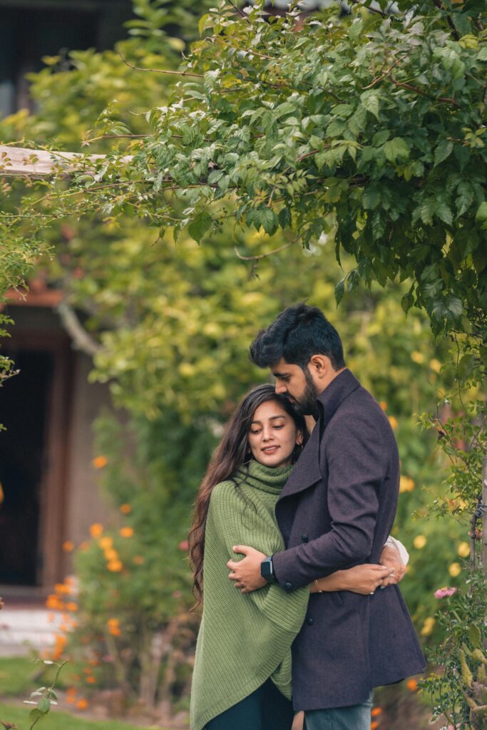 A loving couple embraces in a vibrant garden in UT, India, exuding warmth and romance.